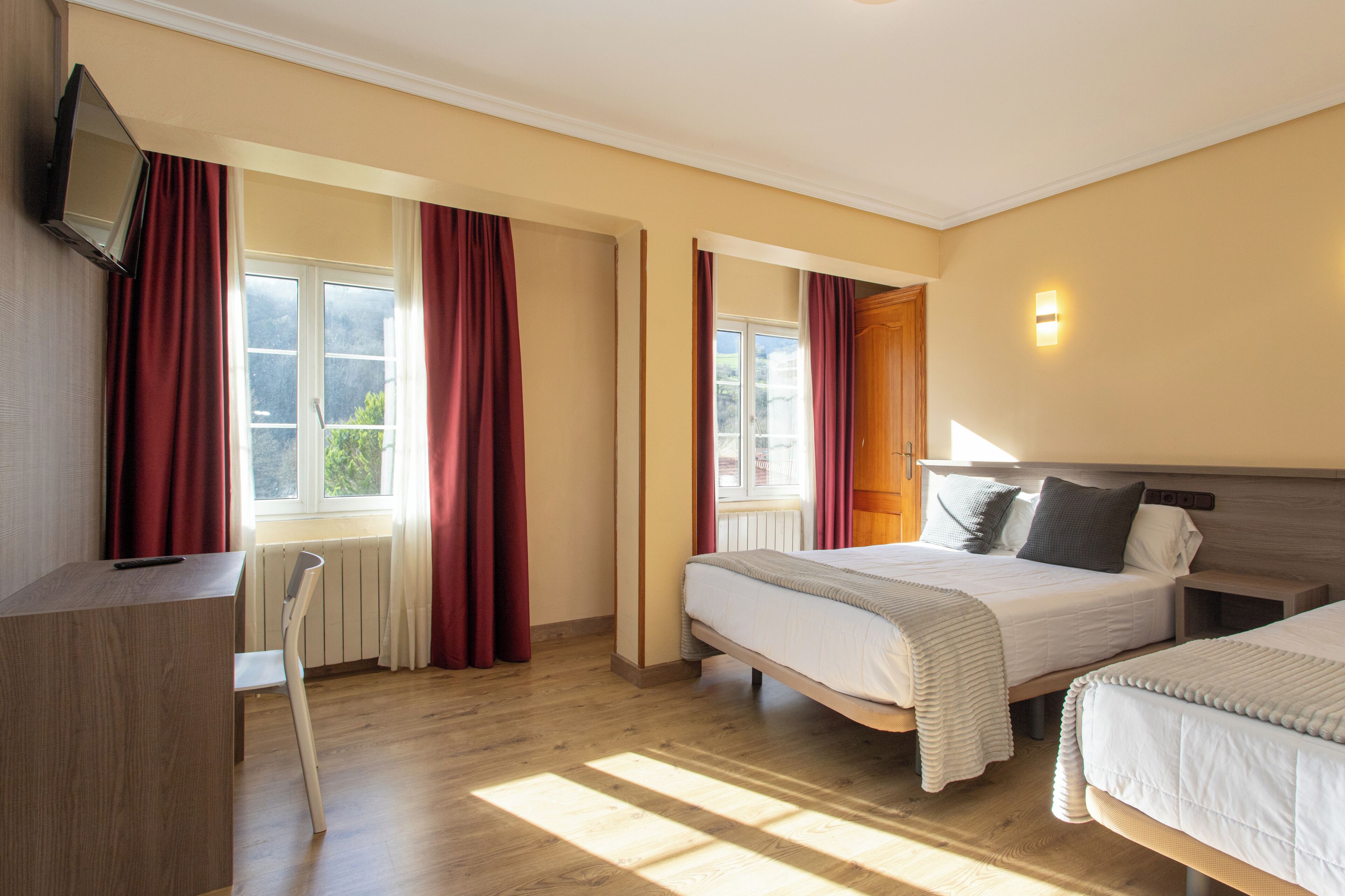 A hotel room with two beds, a desk, a chair, and a TV mounted on the wall.