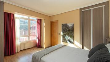 A bedroom with a bed, a window with curtains, a door, and a painting on the wall.