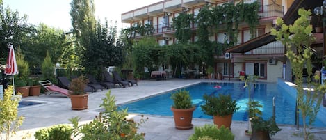 Et hotel med swimmingpool omgivet af krukkeplanter og liggestole.