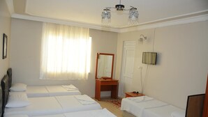 Habitación de hotel con cuatro camas individuales, un escritorio de madera, un espejo, una televisión y una araña.