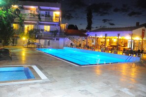 Ein Poolbereich mit einem mosaikgepflasterten Sonnendeck, einem kleinen Pool und einem Gebäude mit Außenbestuhlung und Beleuchtung.