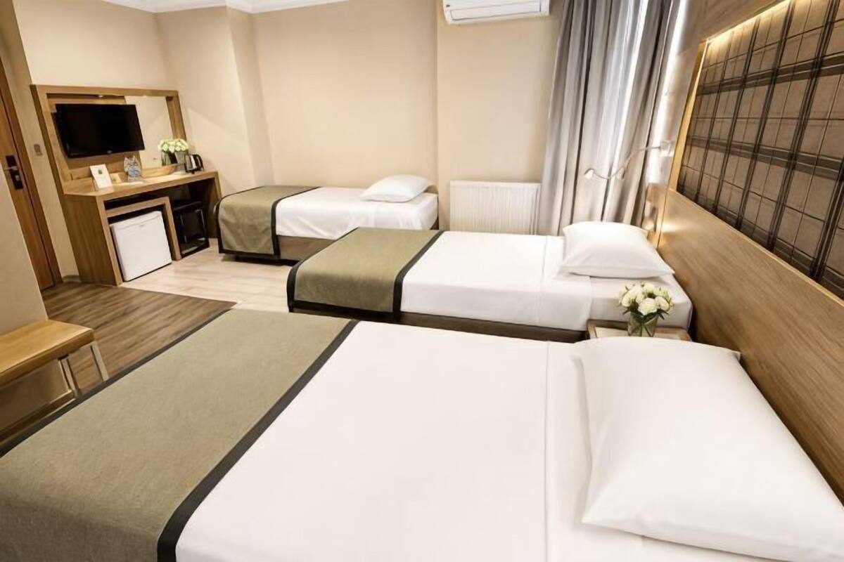 A hotel room with two beds, a desk with a television, and a small kitchenette.