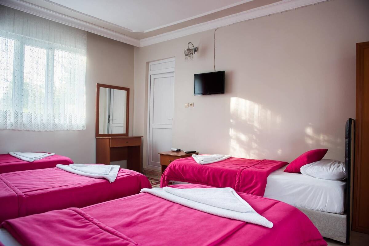 A hotel room with two beds, a vanity with a mirror, a flat-screen TV, and a window with sheer curtains.