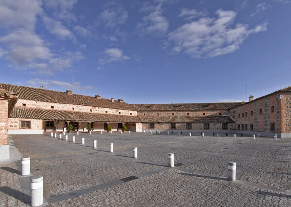 Un patio con edificios de piedra, suelo adoquinado y pilares de defensa.
