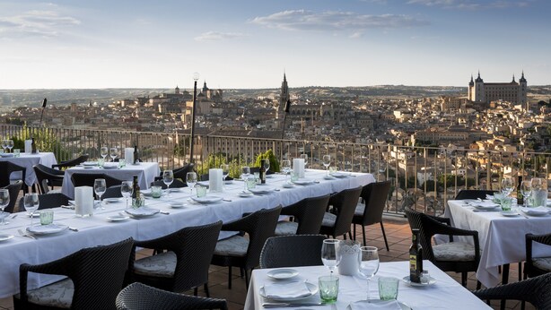 Un restaurante en la azotea con mesas dispuestas para comer, con vistas a un paisaje urbano con edificios históricos.