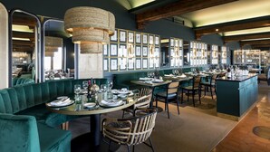 Un restaurante con asientos tapizados en verde, sillas de mimbre y una isla central con barra.