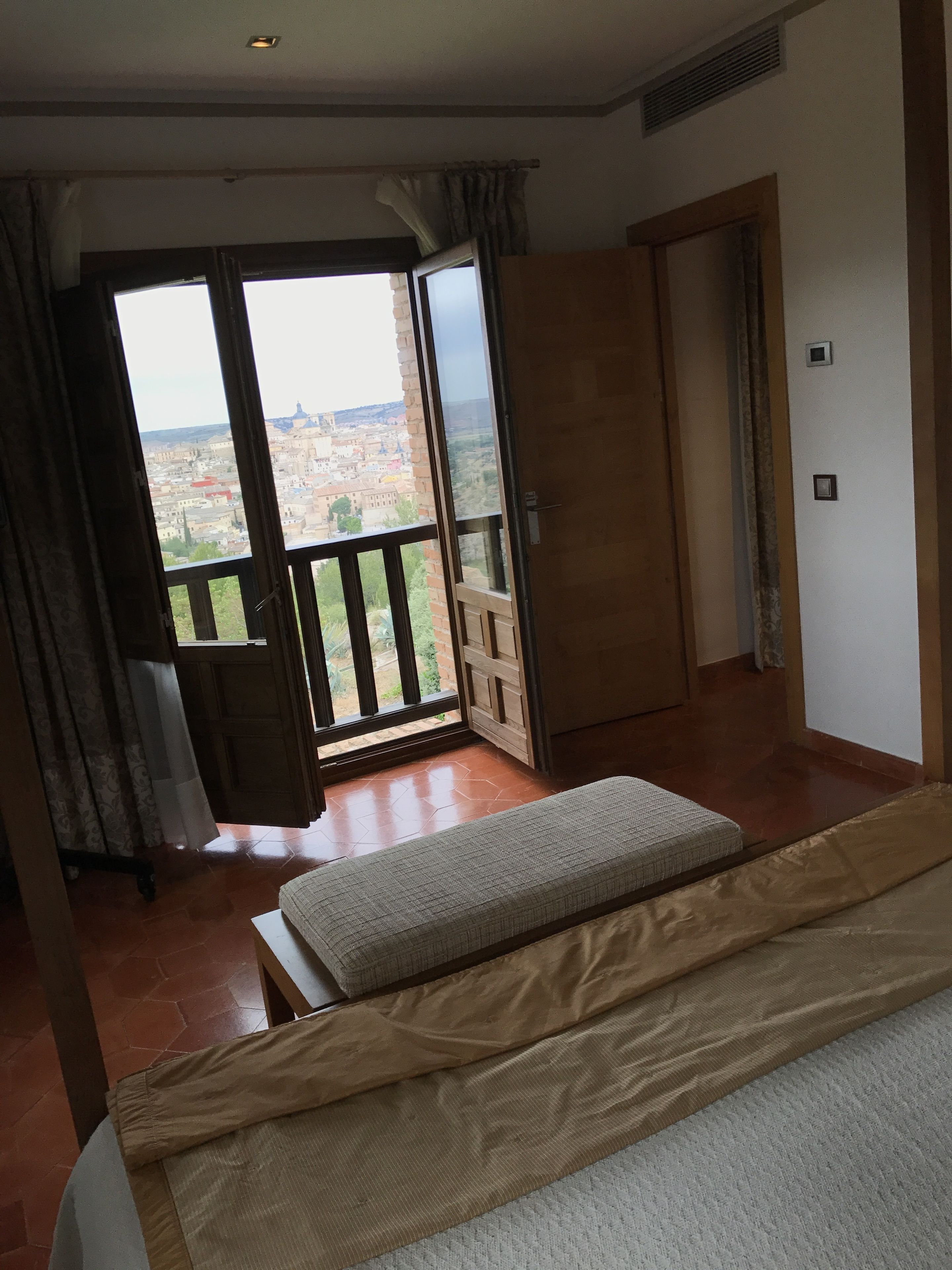 Un dormitorio con un ventanal grande, una cama, un armario de madera y vistas a la ciudad.