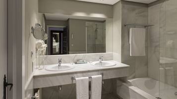 A modern bathroom with two sinks, a large mirror, a glass-enclosed shower, and a bathtub.