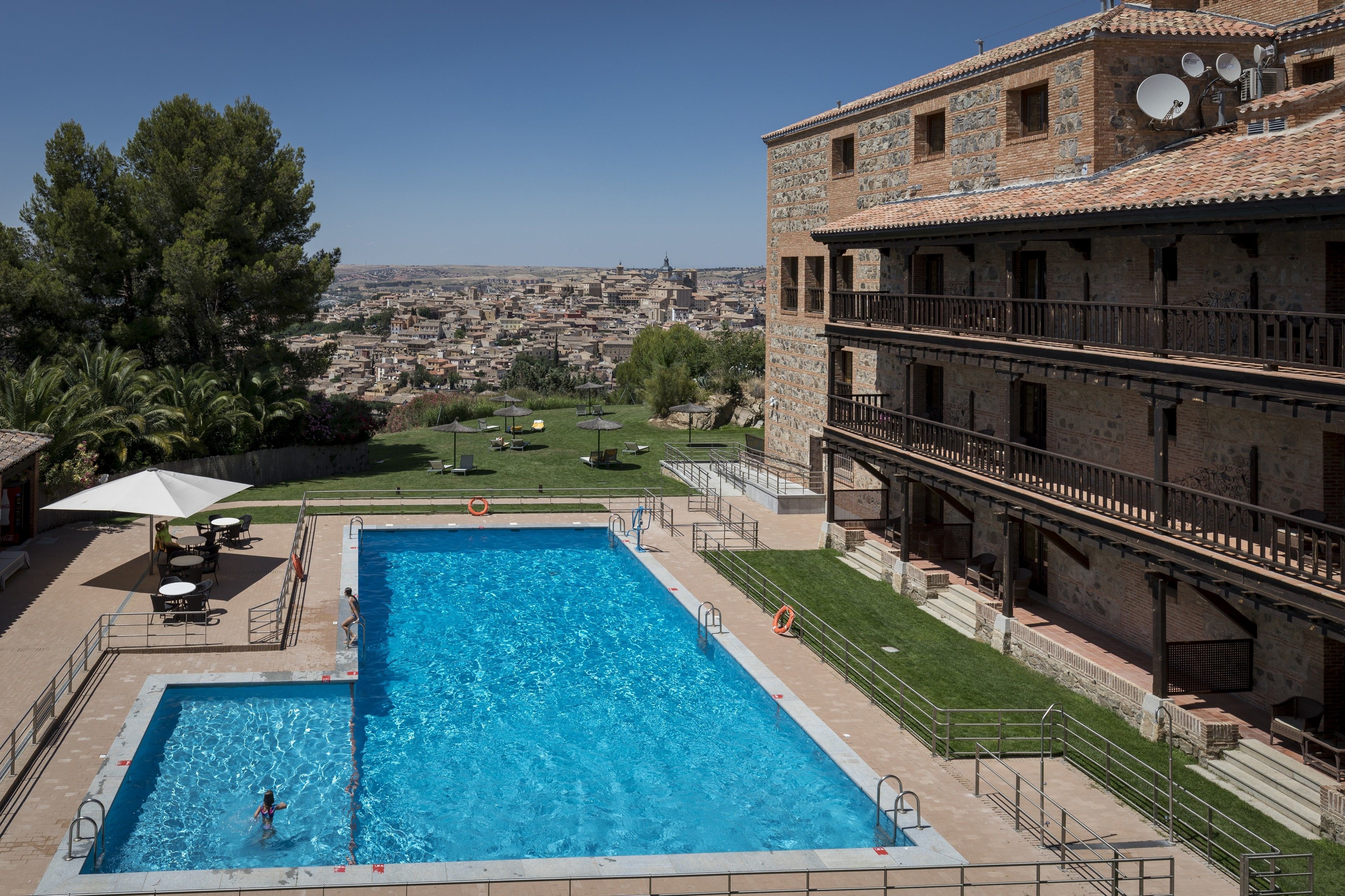 A swimming pool with a view of a cityscape, a covered patio area, and a building with a tiled roof.