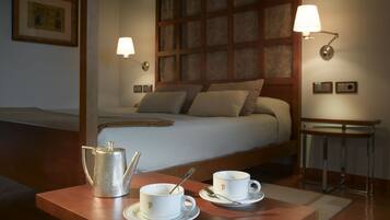 Habitación de hotel con cama, lámparas de noche, una mesita con tetera y tazas, y un cuadro en la pared.