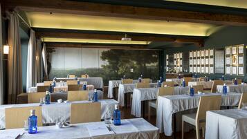 A restaurant with multiple tables set for dining, featuring a mural of trees and a framed picture collection on the wall.