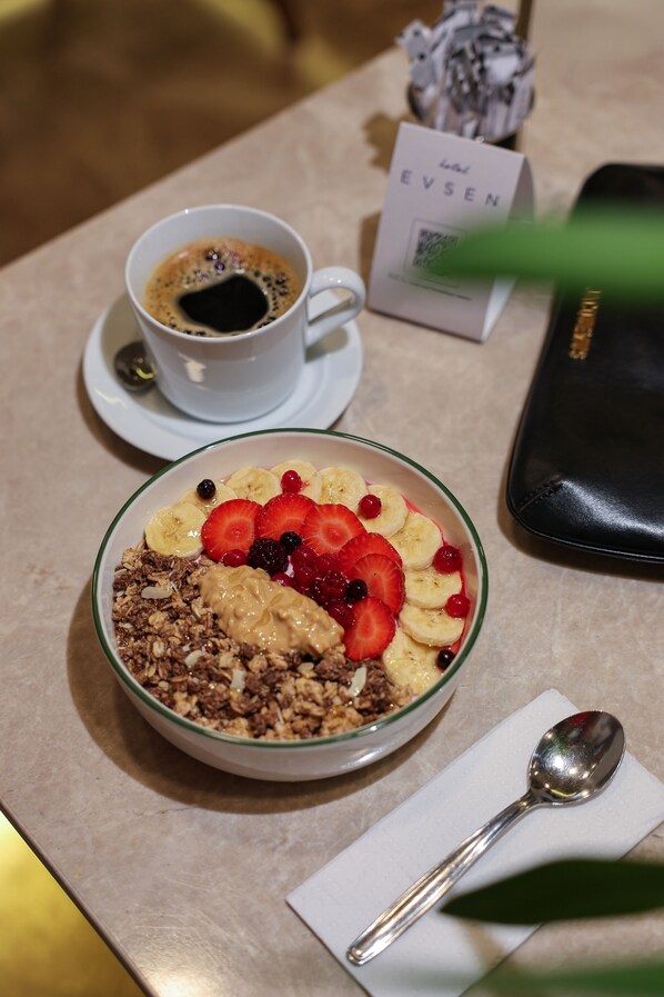 Una mesa con un bol de cereal cubierto de frutas y una taza de café.