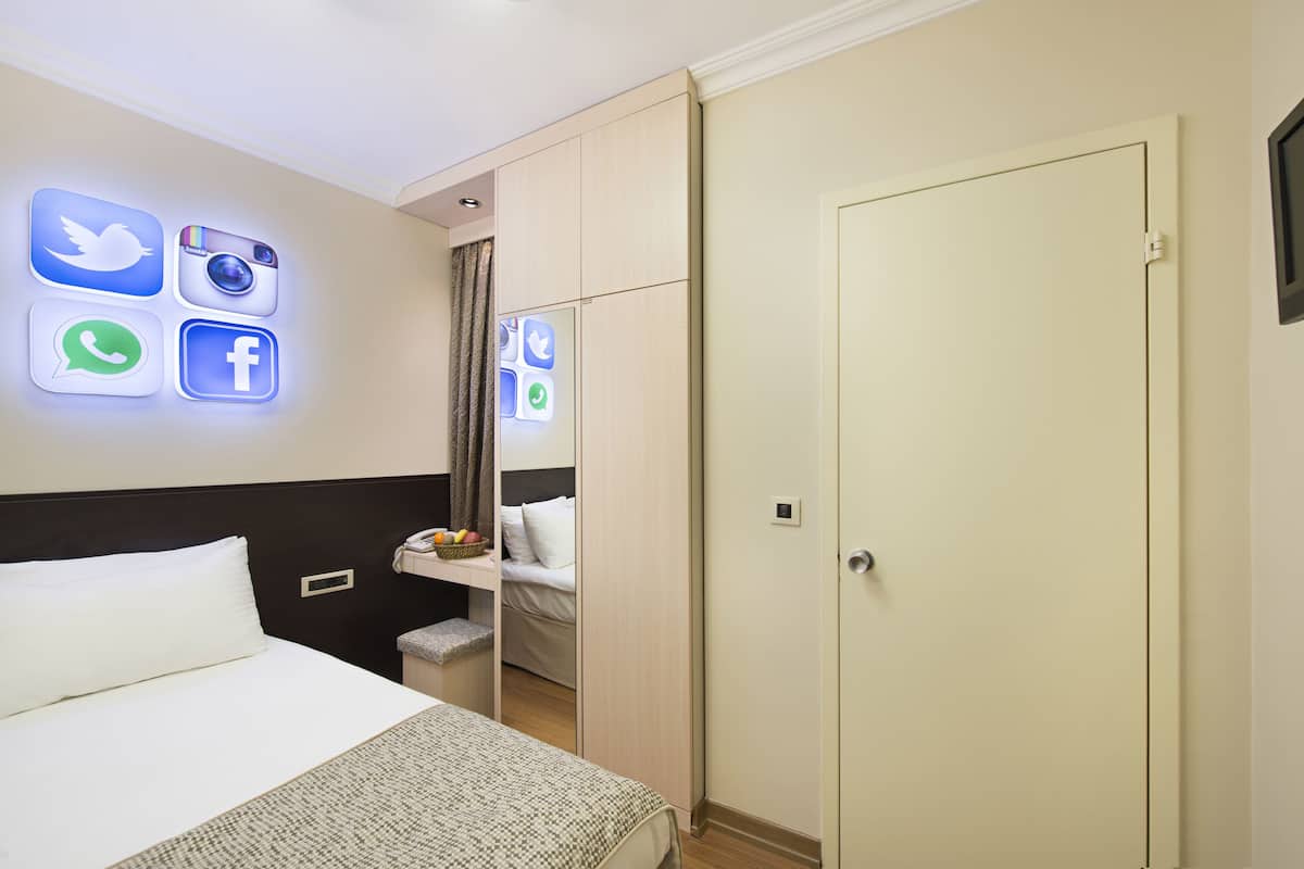 Habitación de hotel con cama, mesita de noche con frutero, armario y pared con iconos iluminados de redes sociales.