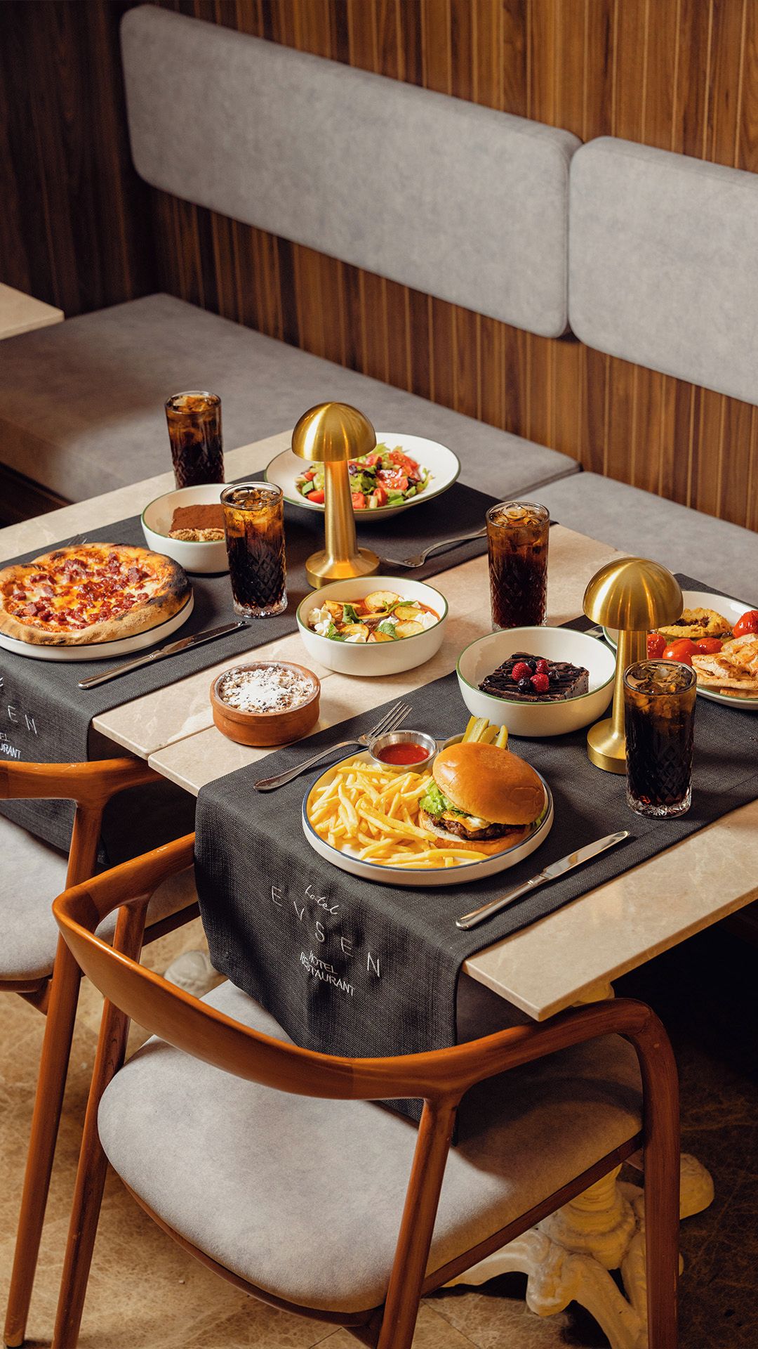 Una mesa de comedor dispuesta con diferentes platos, bebidas y una lámpara.