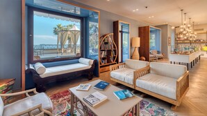 A modern living room with a large window, a bookshelf, a sofa, and a table with books. - Villa Capri (Gardone Riviera)