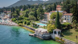 A coastal hotel with a swimming pool, lush greenery, and a view of the sea. - Villa Capri (Gardone Riviera)