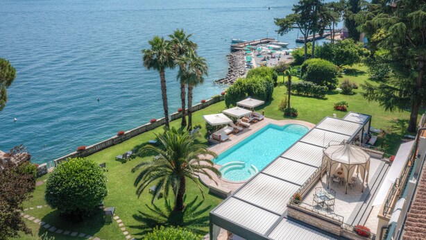 A pool with a view of the sea, a gazebo, and a deck with lounge chairs. - Villa Capri (Gardone Riviera)