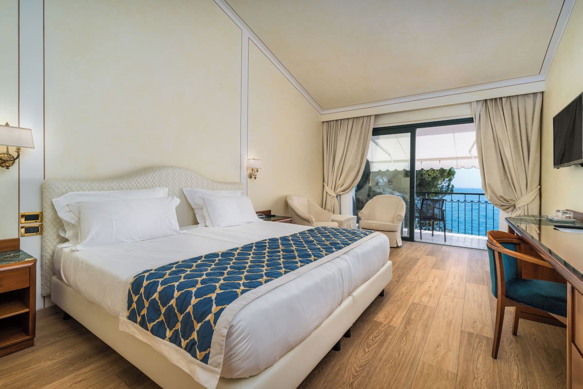 A hotel room with a bed, a desk, a chair, and a balcony with a view.