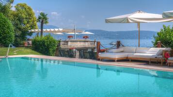 Ein Swimmingpool mit Liegestühlen und Sonnenschirmen, ein Tisch mit Blumen sowie Meer- und Bergblick.