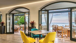 A modern dining area with a table and chairs, large windows with curtains, and a view of the sea. - Villa Capri (Gardone Riviera)
