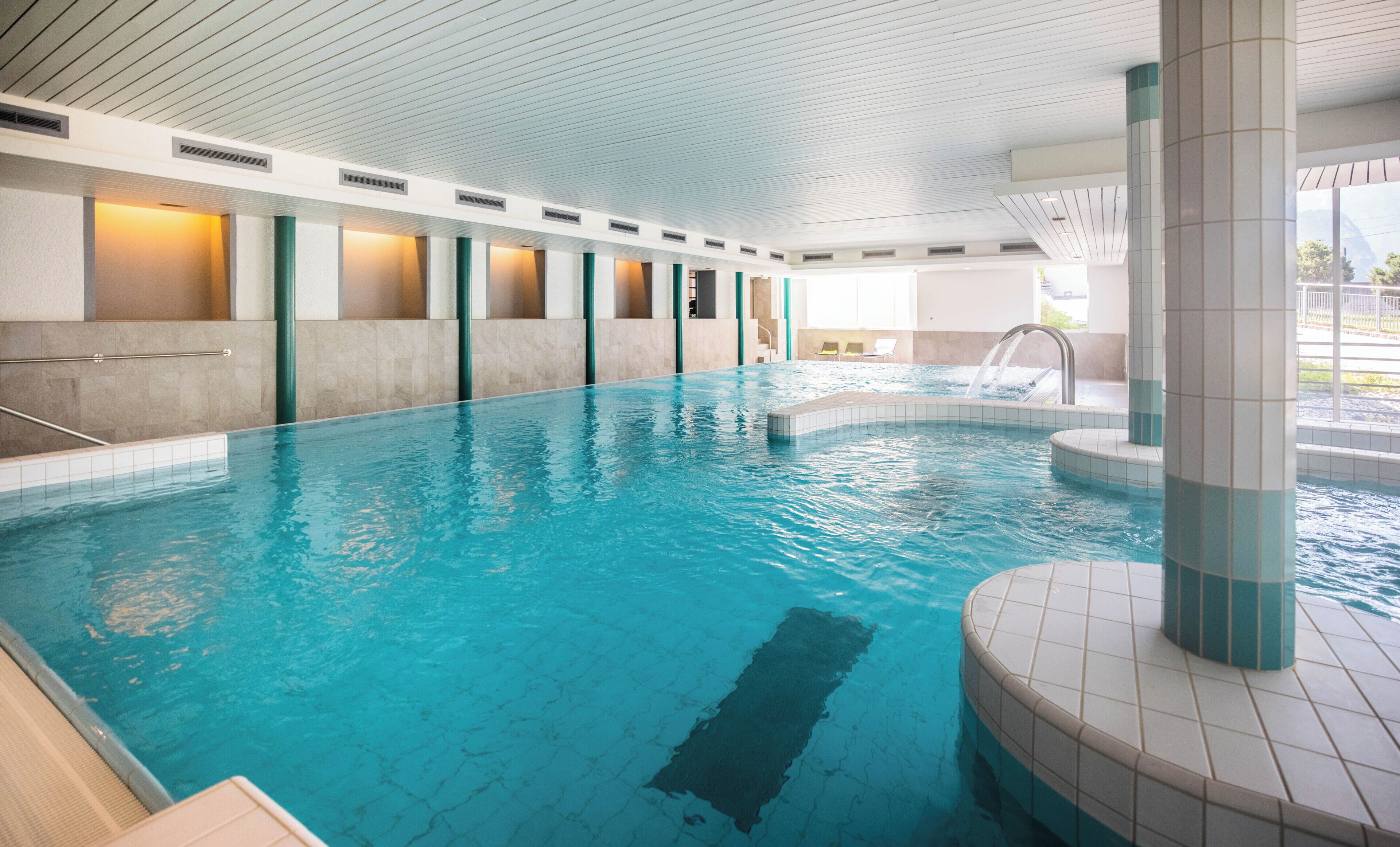 An indoor swimming pool with a tiled floor and a series of columns.