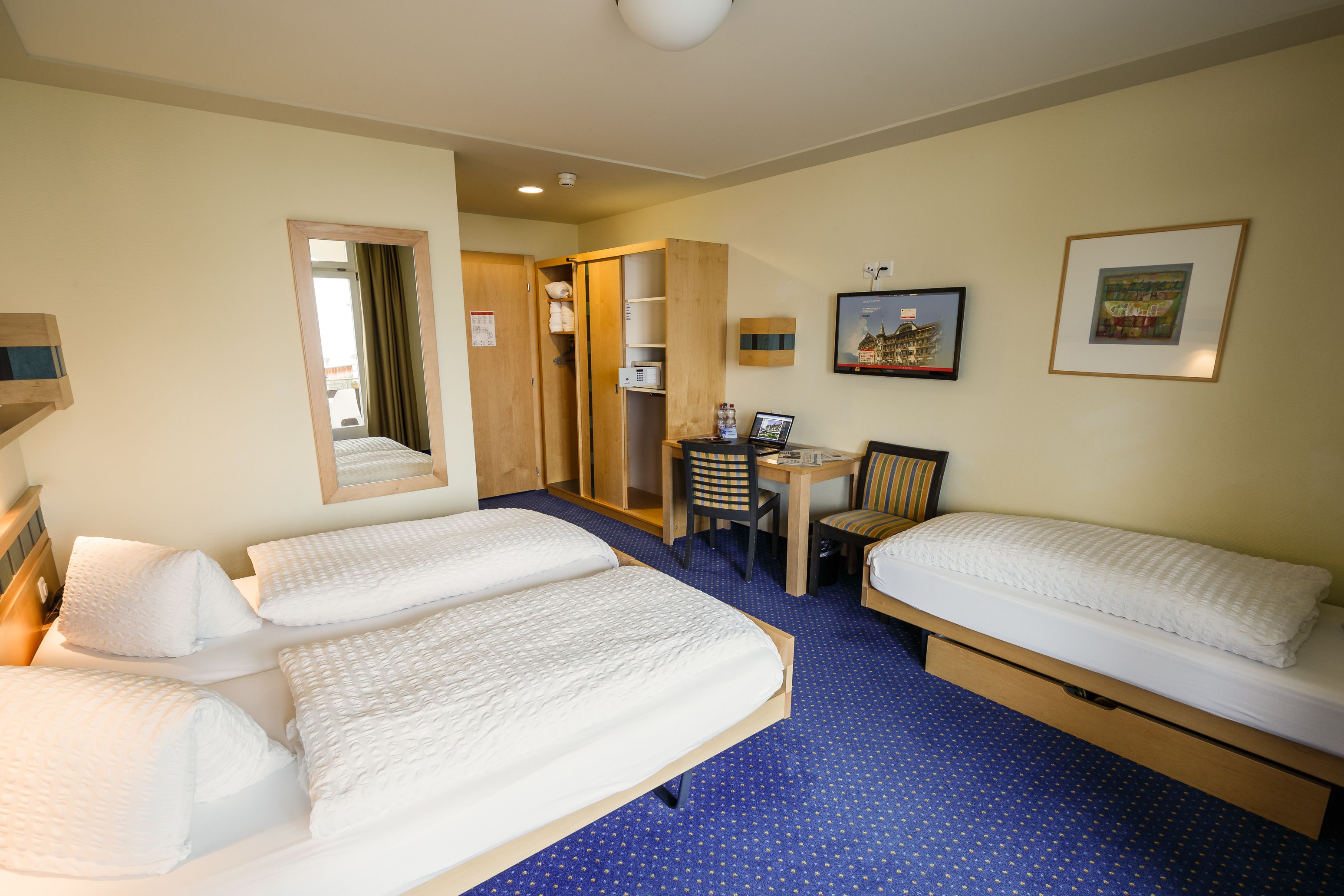 Habitación de hotel con dos camas, un escritorio, una silla y un armario.
