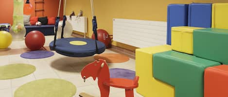 A playroom with colorful mats, a rocking horse, and soft play furniture.