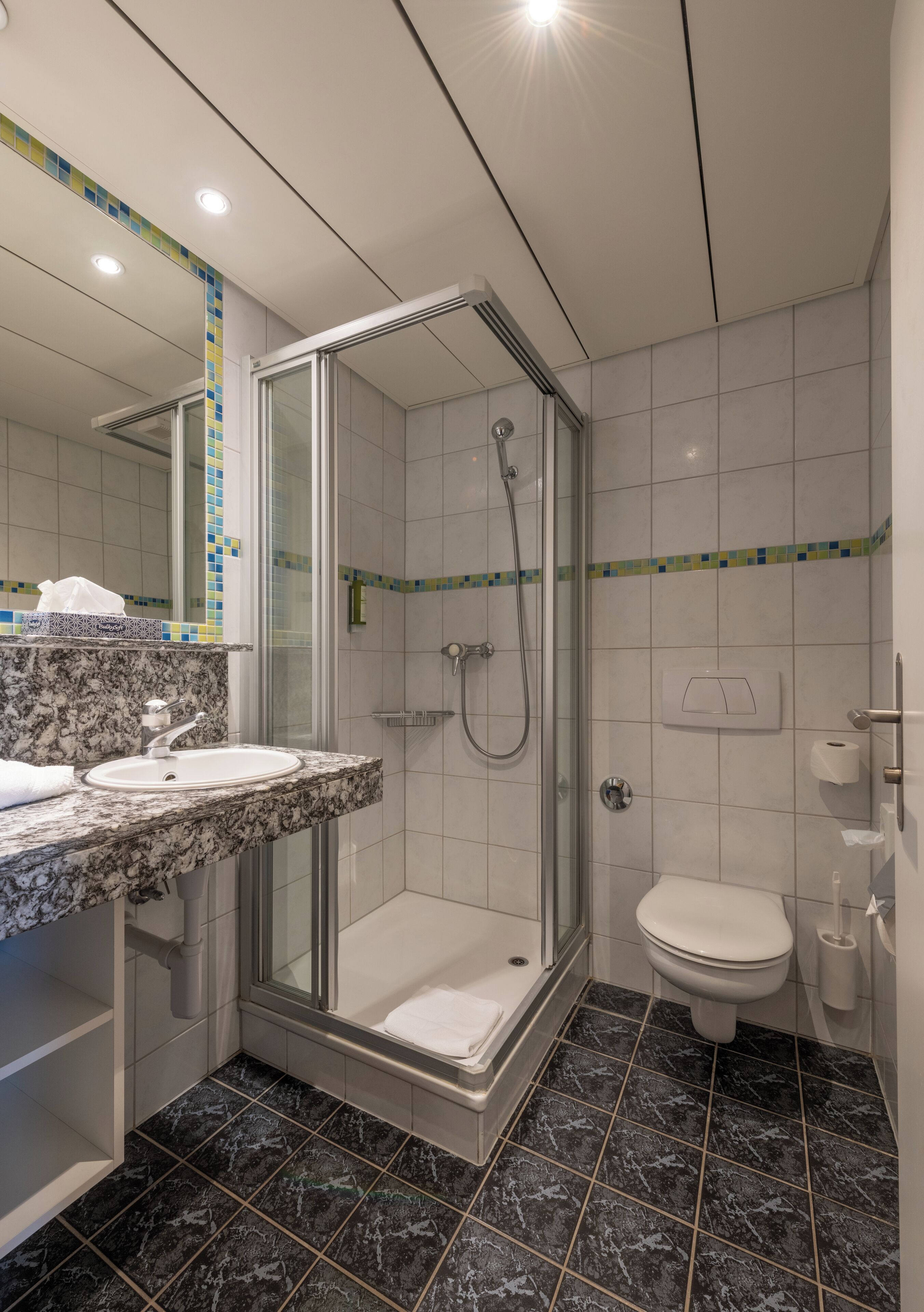 Ein modernes Badezimmer mit einer gläsernen Duschkabine, einem Marmorwaschbecken und einer weißen Toilette.