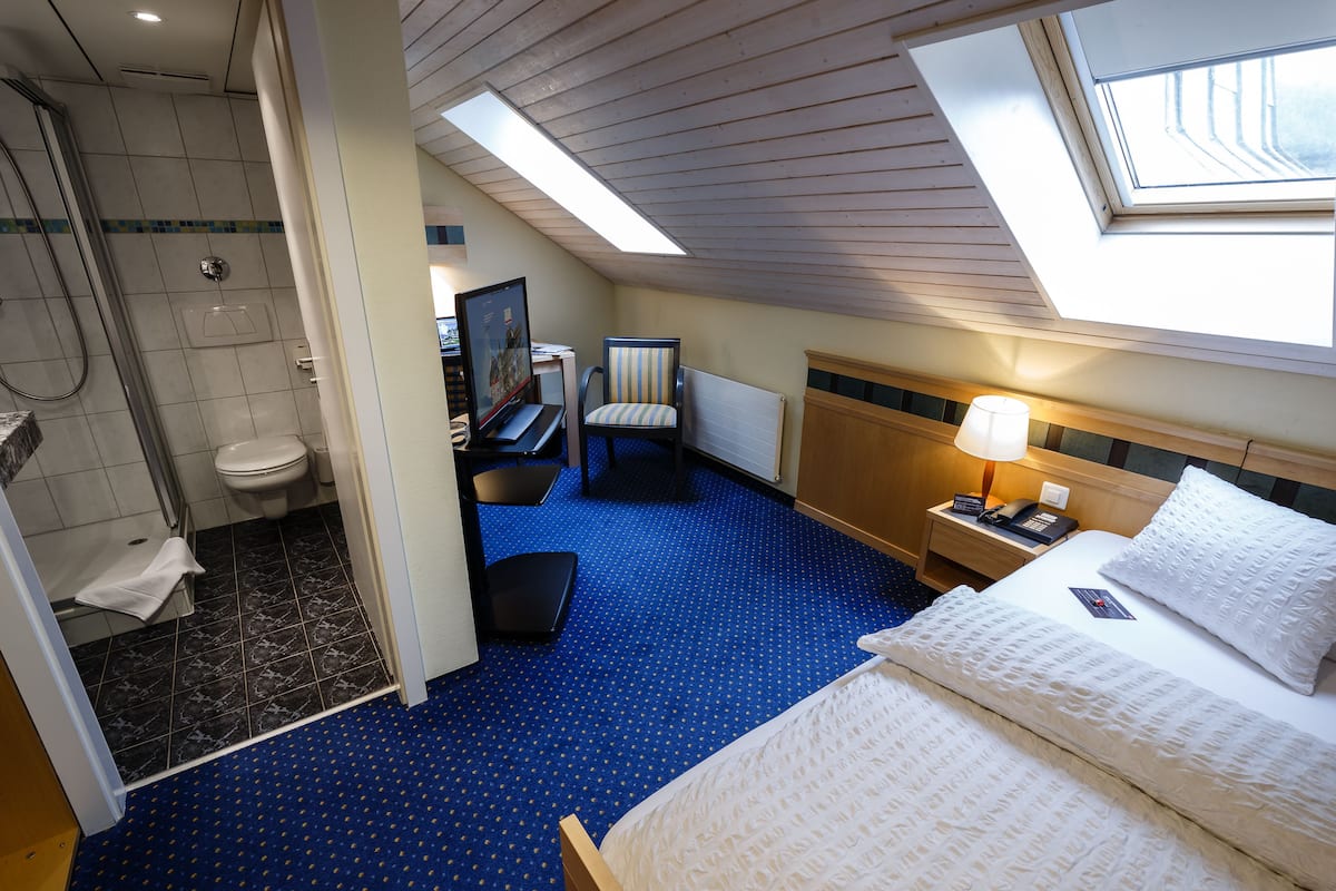 Ein Hotelzimmer mit Oberlicht, Dusche, Bett, Schreibtisch und Stuhl.