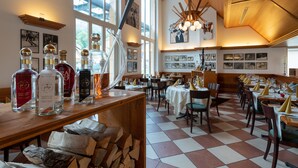 Een restaurant met een geruit vloertje, houten tafels, stoelen en verschillende flessen op een toonbank.