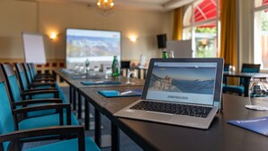 Een vergaderruimte met een lange tafel, stoelen, een laptop en een projectiescherm.