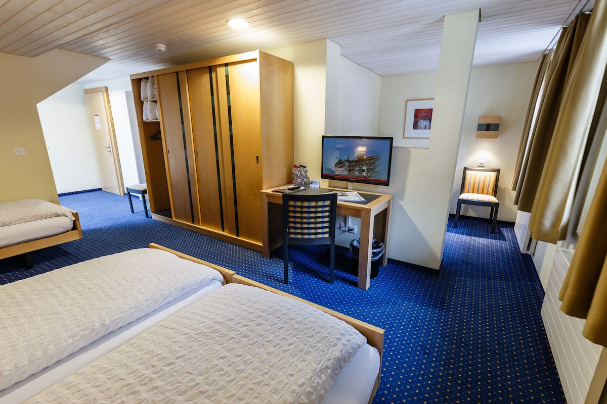 Ein Hotelzimmer mit zwei Betten, einem Schreibtisch mit Computer, einem Stuhl, einem Kleiderschrank und einem Fernseher.