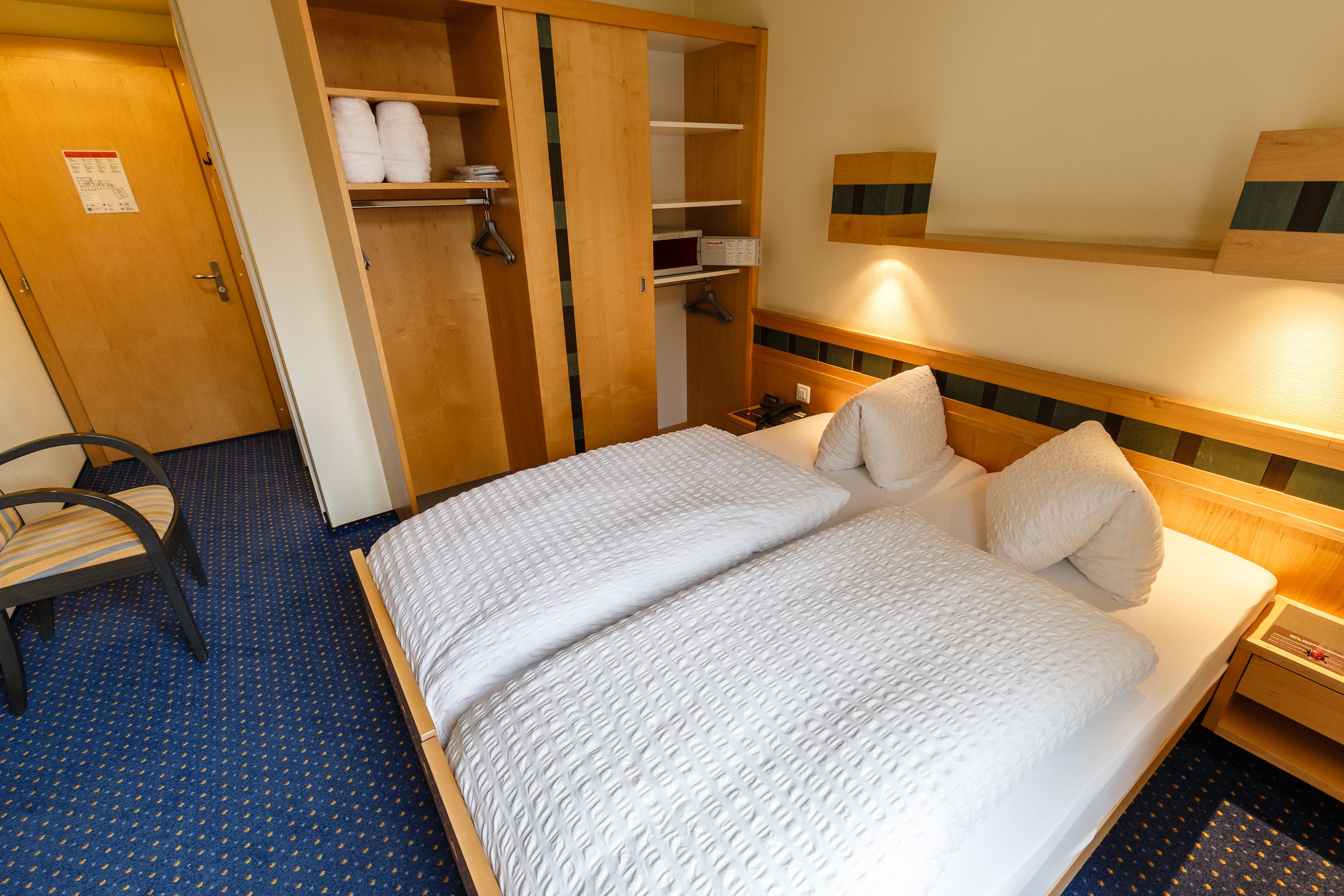 A hotel room with a bed, a chair, a wardrobe, and a nightstand.