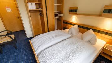 Una habitación de hotel con cama, una silla, un armario y una mesita de noche.