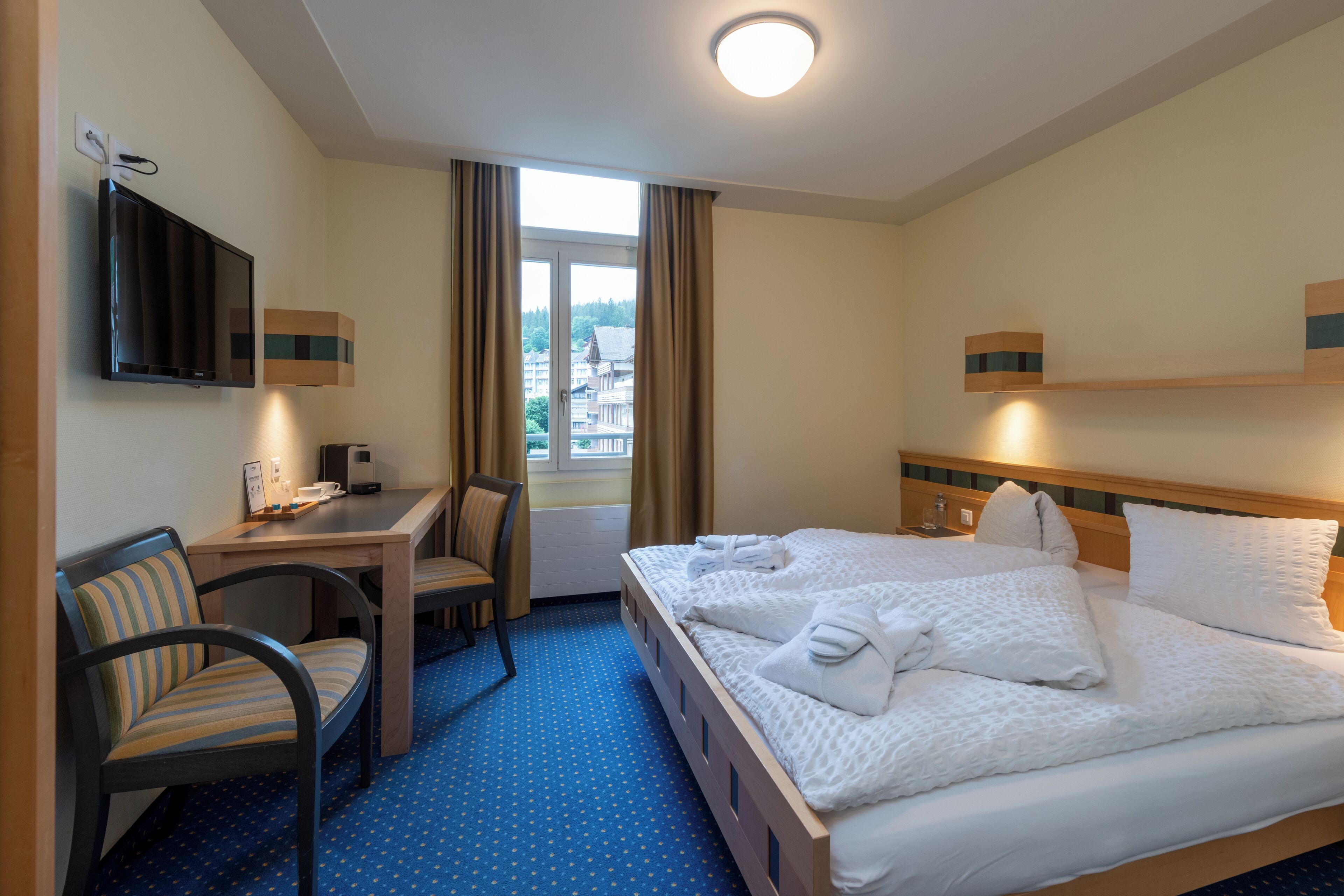 A hotel room with a bed, a desk, a chair, and a TV.