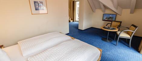 Habitación de hotel con dos camas, una mesita con sillas, un cuadro en la pared y una escalera que lleva a otra habitación.