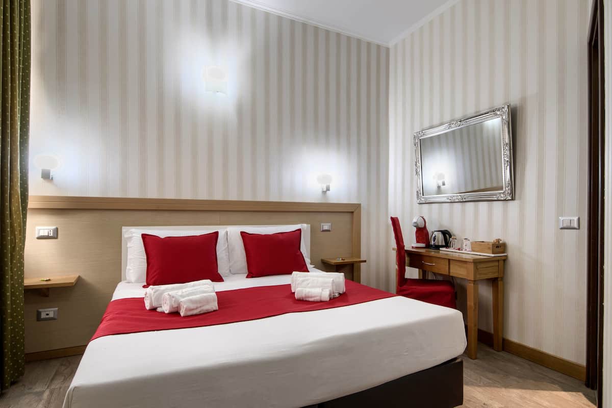 Une chambre d’hôtel avec un grand lit, des oreillers rouges, un bureau en bois, un miroir et une chaise rouge.