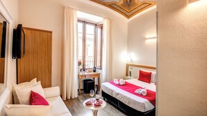 A hotel room with a wooden desk, a bed with red bedding, a white sofa, and a ceiling with intricate designs. - Auditorium Mecenate (Rome)
