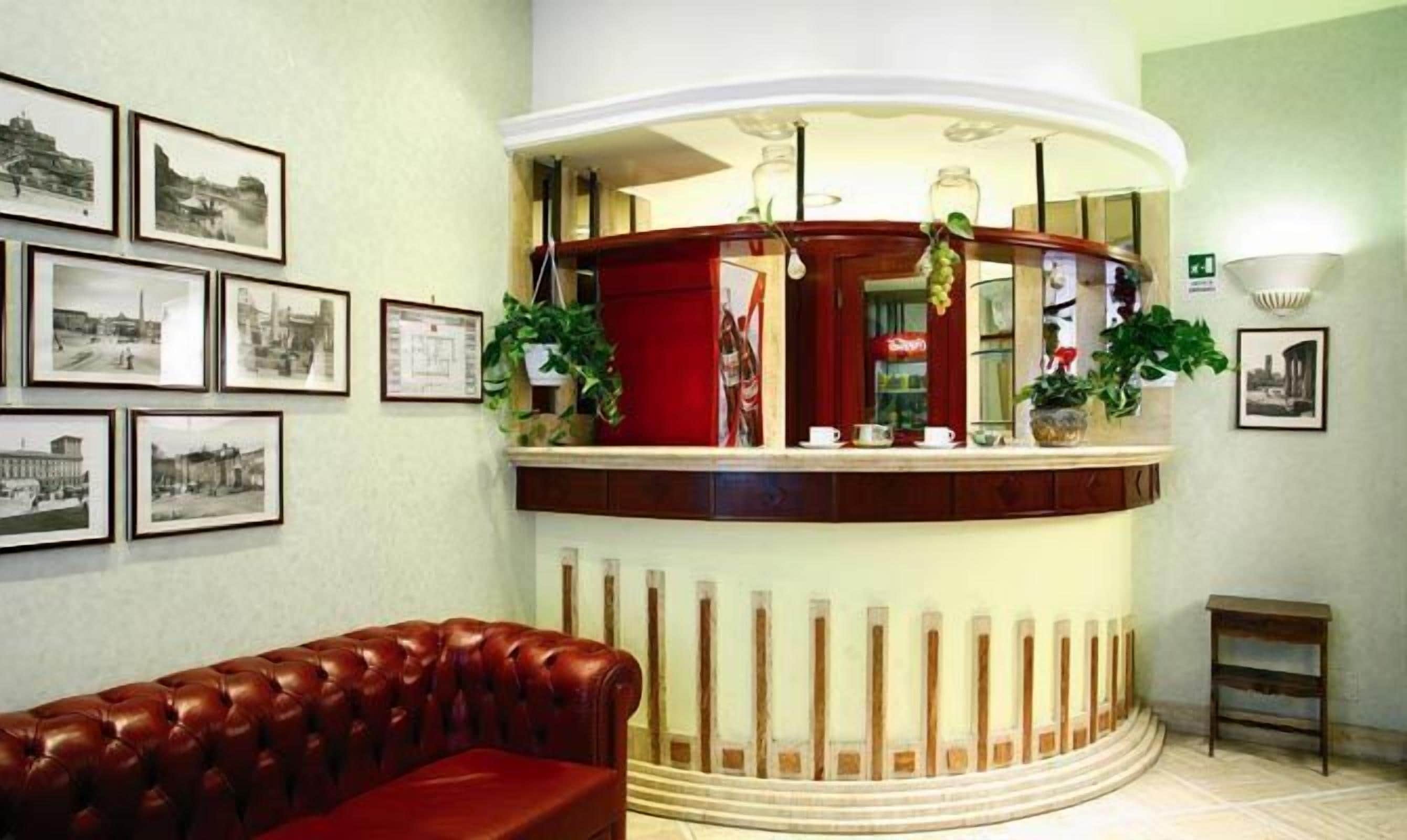 A reception area with a red leather couch, a reception desk with a red backdrop, and framed black and white photographs on the wall.