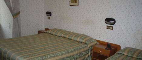 A room with two beds, each with a striped bedspread, a wooden nightstand, and a wall-mounted telephone.