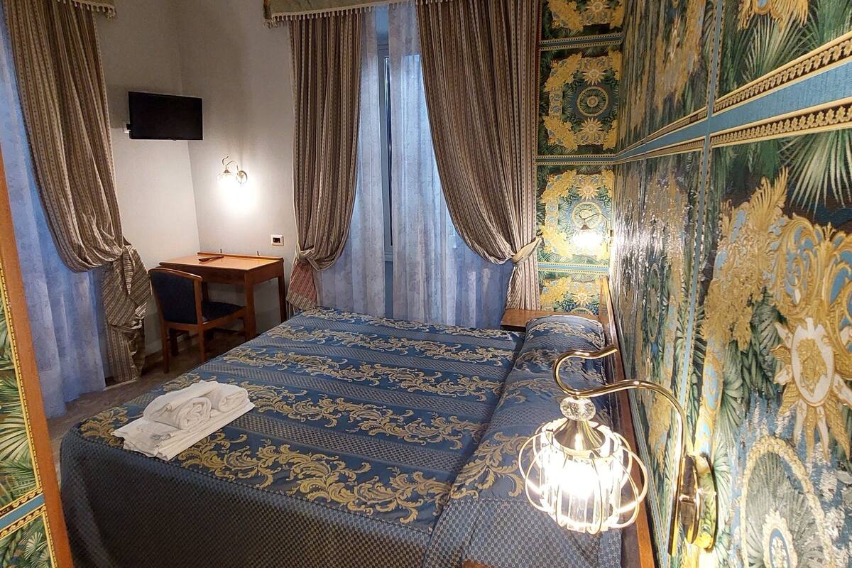 A bedroom with a large bed, curtains, a desk, and a TV.
