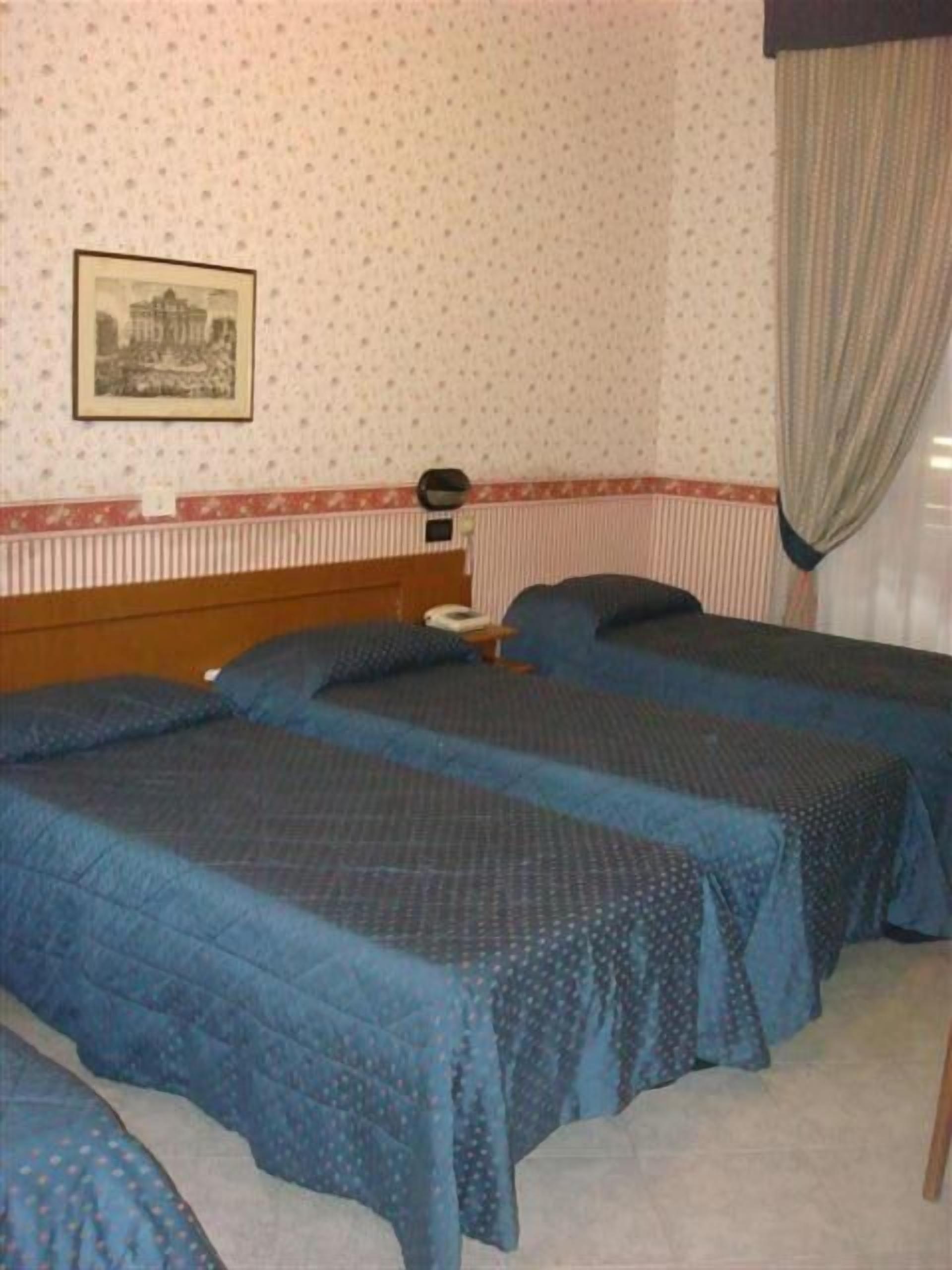 Een kamer met twee bedden, een nachtkastje, een lijst met een afbeelding aan de muur en een gordijn.