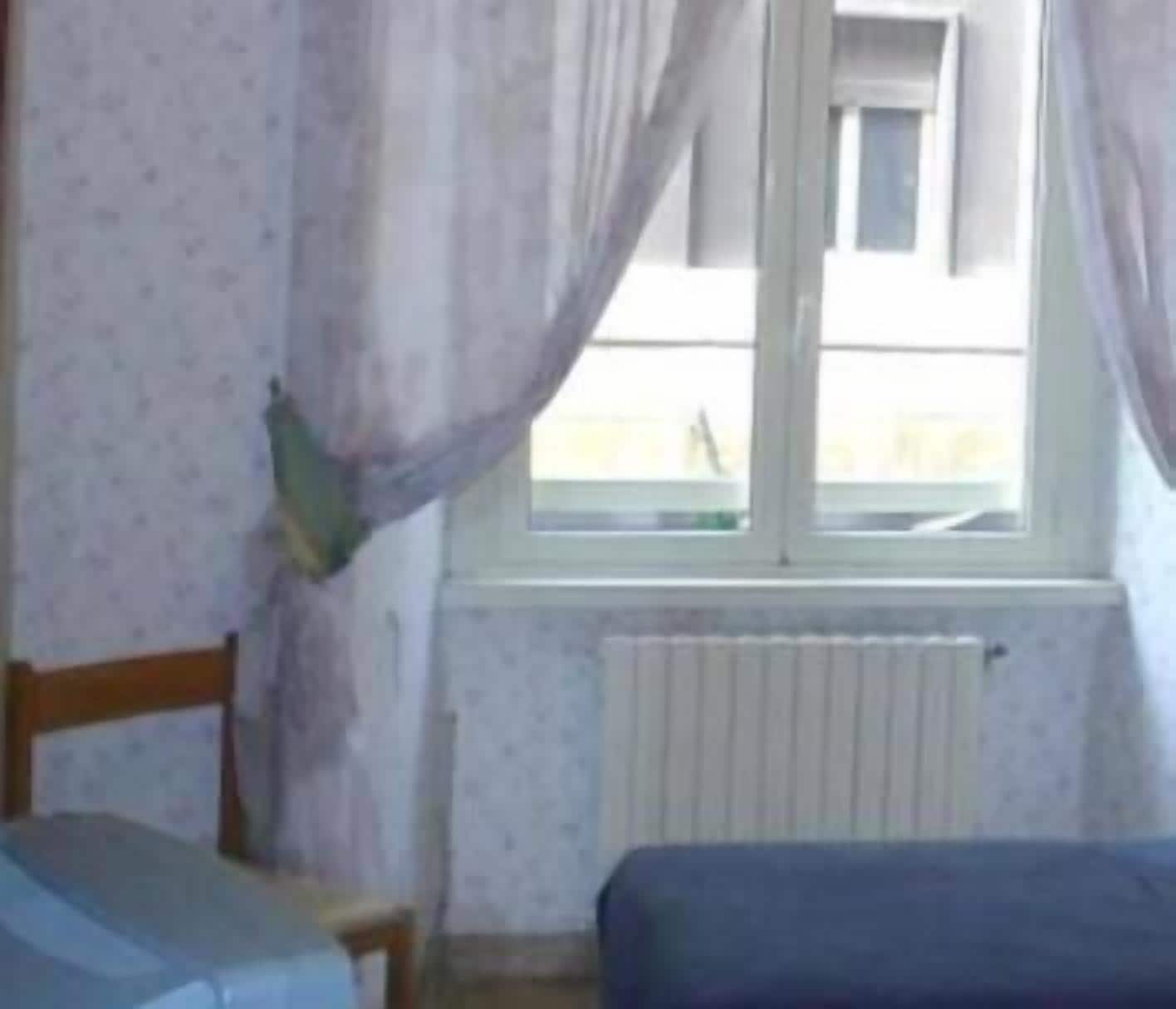 A room with a bed, a chair, a window with curtains, and a radiator.