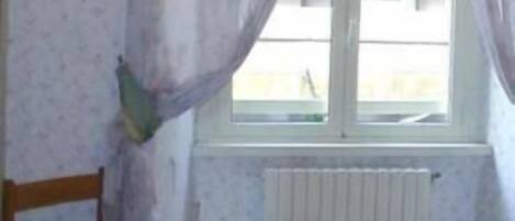 A room with a bed, a chair, a window with curtains, and a radiator.