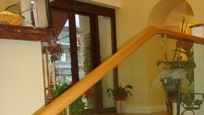 A staircase with glass railings and wooden handrails, leading to a landing with potted plants and a decorative item. - Hotel Demetra Capitolina (Rome)