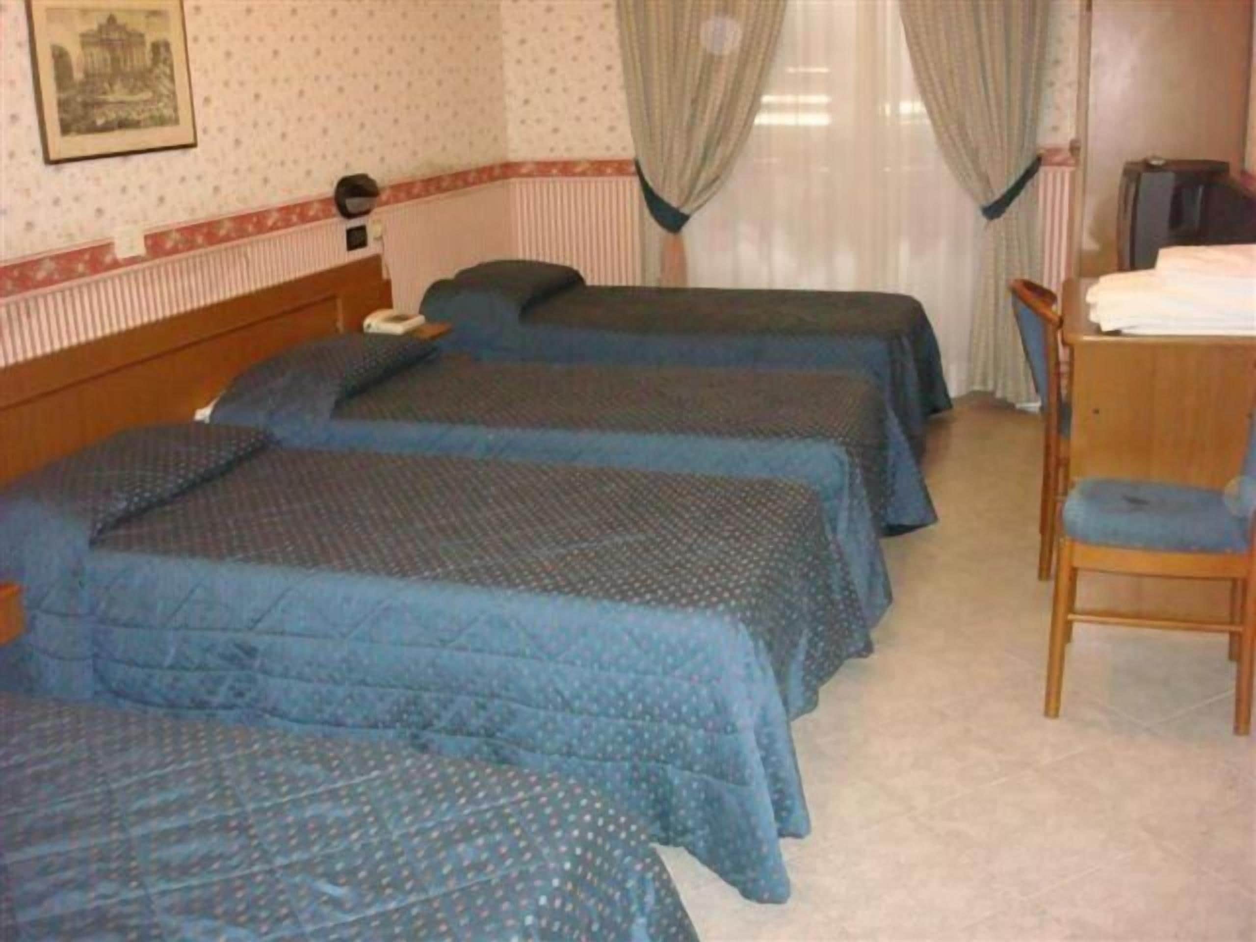 A hotel room with three single beds, a wooden desk, and a chair.