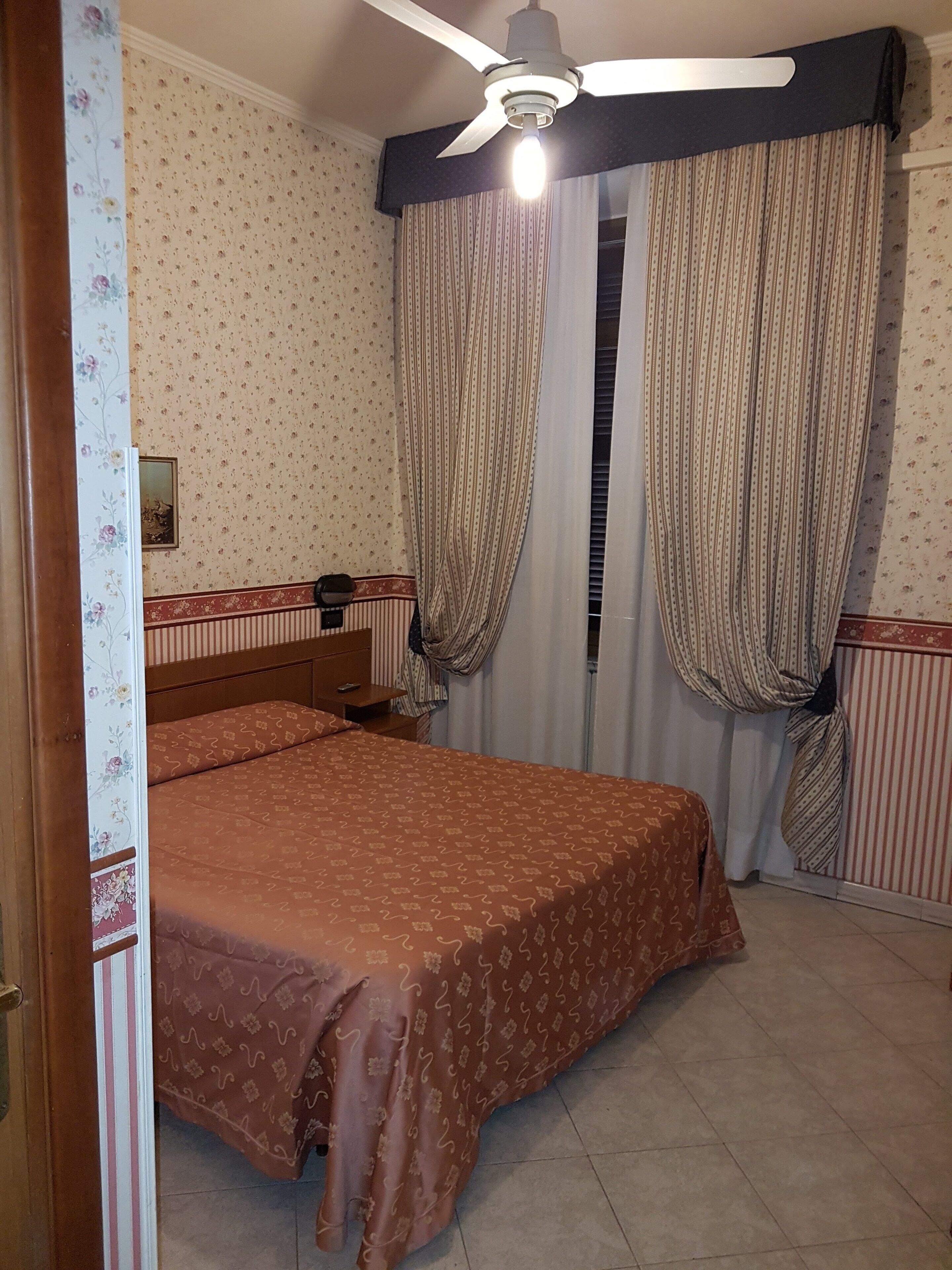 Ein Schlafzimmer mit Bett, Vorhängen, Deckenventilator und Fenster mit Jalousien.