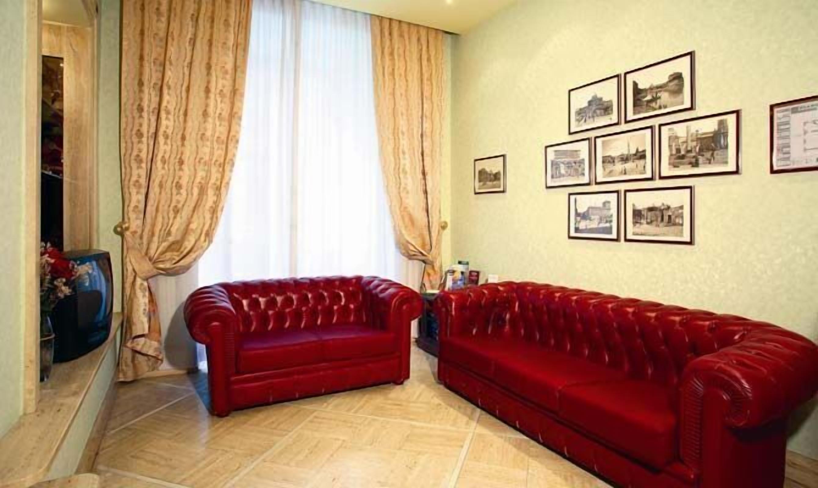 Una sala de estar con dos sofás rojos, un ventanal con cortinas y varias fotografías enmarcadas en la pared.
