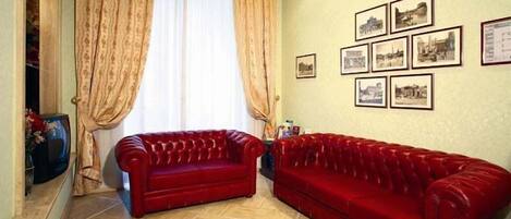 Una sala de estar con dos sofás rojos, un ventanal con cortinas y varias fotografías enmarcadas en la pared.
