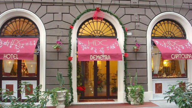 A hotel facade with three arched windows, each with a pink awning displaying the hotel's name. - Hotel Demetra Capitolina (Rome)